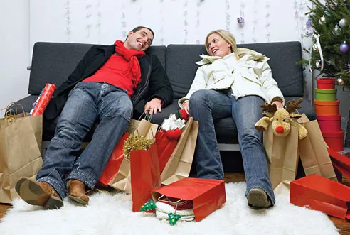 Couple relaxing on a couch surrounded by holiday gifts and decorations.