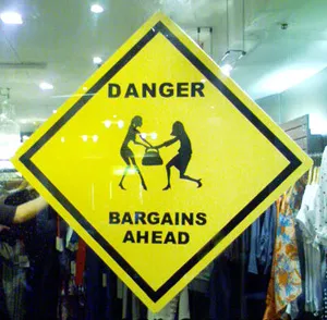 Warning sign indicating "Danger: Bargains Ahead" with two figures reaching for a shopping bag.