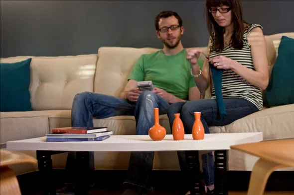 A couple sitting on a couch, engaged in a craft project with colorful vases on the coffee table.