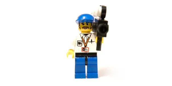 Lego minifigure holding a camera, wearing a blue hard hat and a press badge.
