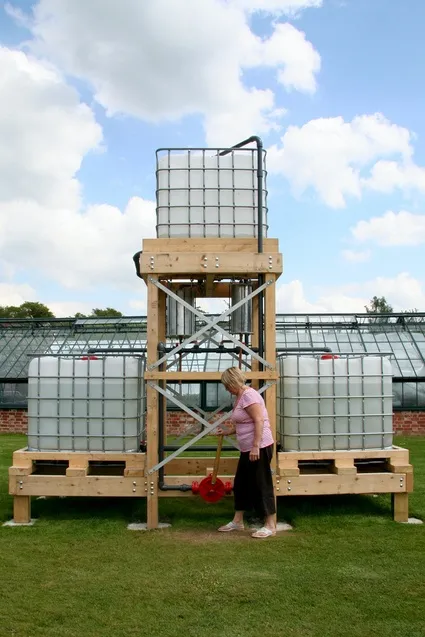 Woman operating a water collection system with large storage tanks outdoors.