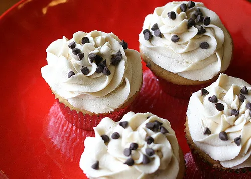 Chocolate chip cupcakes with vanilla frosting on a red plate.