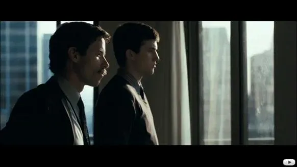 Two men in business suits standing by a window, looking out at a city skyline.