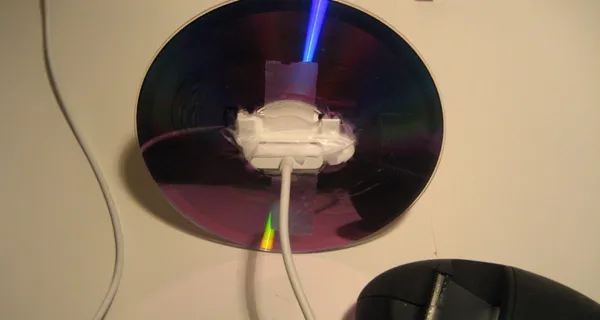 A reflective CD placed against a surface with a white cable attached.