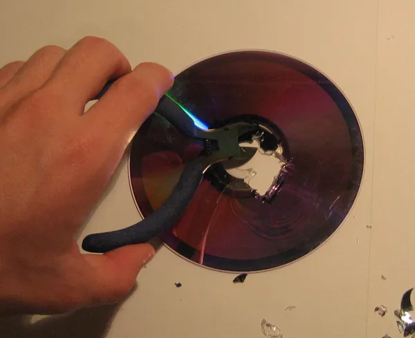 Hand using pliers to break a CD.