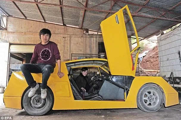 A young man sits on the edge of a modified yellow car with its door open in a garage setting.