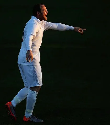 A soccer player in a white uniform gestures intensely on the field.