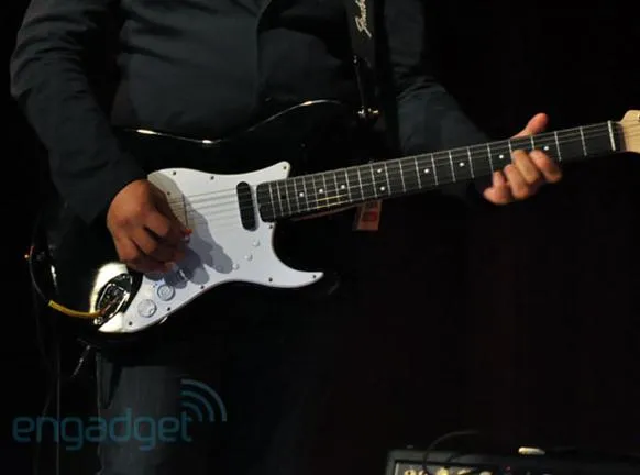 Hand playing a black electric guitar on stage.