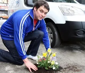 Man kneeling beside a flower arrangement on the ground near a van.