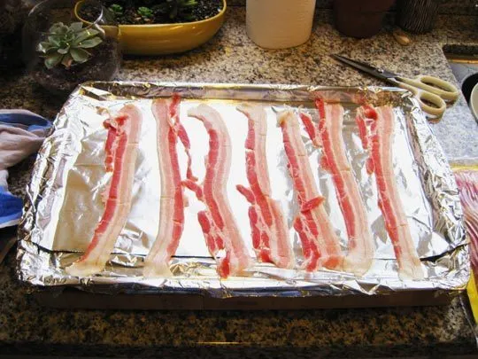 Cooked bacon strips arranged on a foil-lined baking sheet.