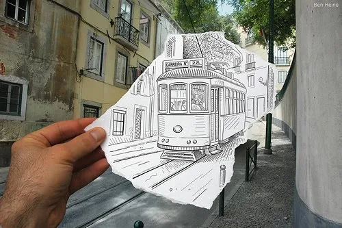 A hand holding a sketch of a tram in a street setting.