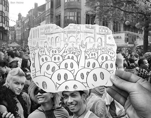 A hand holding a drawing of a crowd amidst a larger crowd at a public event.