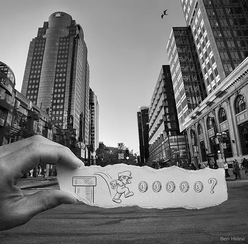 A hand holding a torn piece of paper with a drawing in an urban setting.