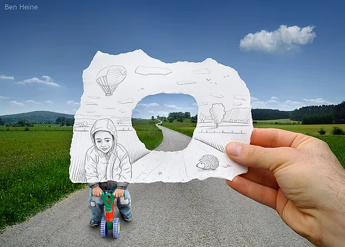 A hand holding a torn piece of paper with a drawing of a person, set against a scenic landscape featuring a road and clouds.