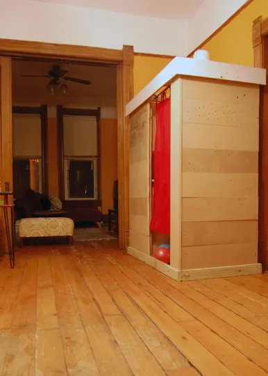 Interior view of a room featuring wooden floors, a seating area, and a partitioned space with a red curtain.
