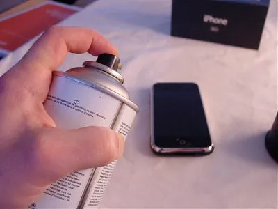 Hand holding a spray can near a smartphone.