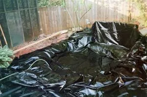 Black plastic liner placed in a backyard for a pond or gardening project.