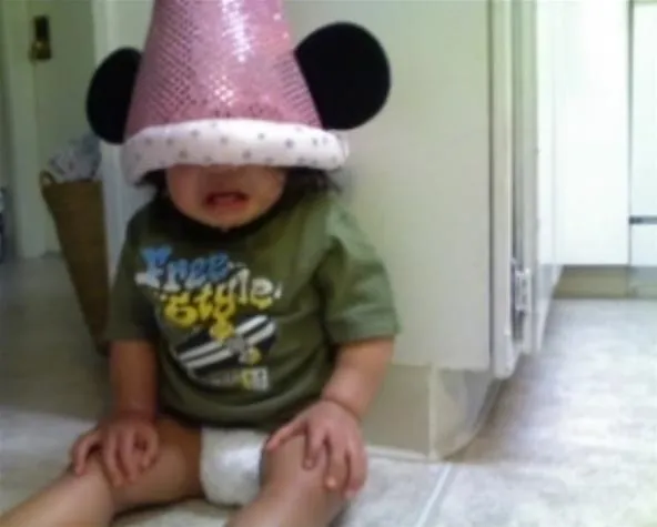 Child wearing a pink Minnie Mouse hat sitting on the floor.