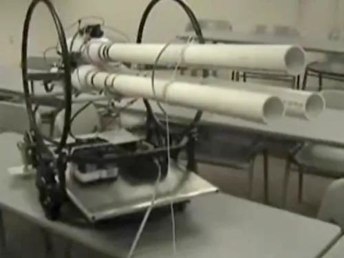 Robot equipped with dual launchers on a table in a classroom setting.