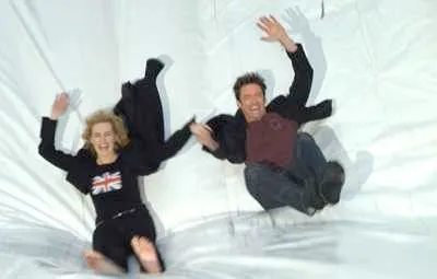 A man and a woman joyfully sliding down a white surface.