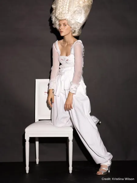 Fashion model in avant-garde white outfit and dramatic hairstyle sitting on a chair.