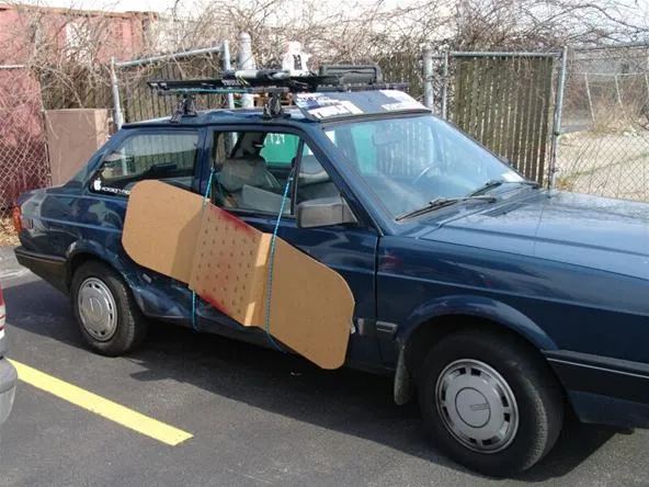 Car with makeshift cardboard door repair parked in a lot.