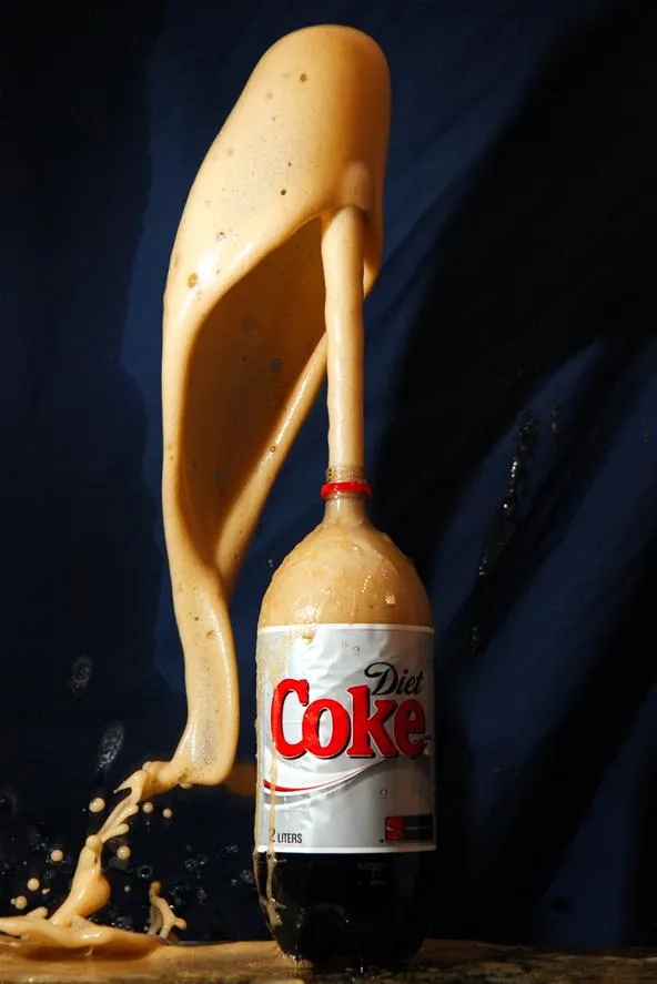 Diet Coke bottle with a foamy eruption against a dark background.