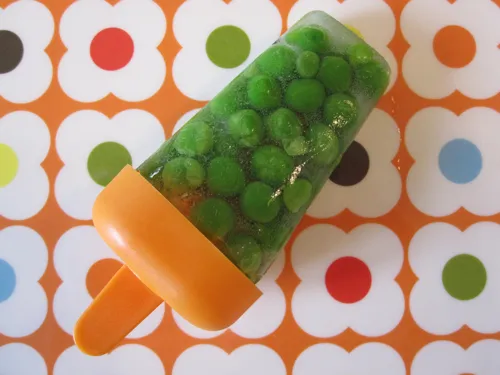 Green peas in a popsicle mold on an orange and white patterned background.