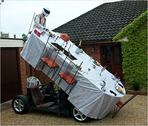 A car designed to look like a dining table with a tablecloth and food, showcased in a driveway.