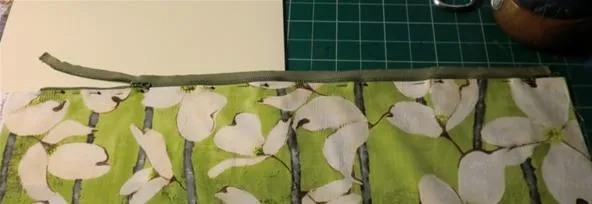 Fabric with a green and white leaf pattern next to a blank piece of paper on a cutting mat.