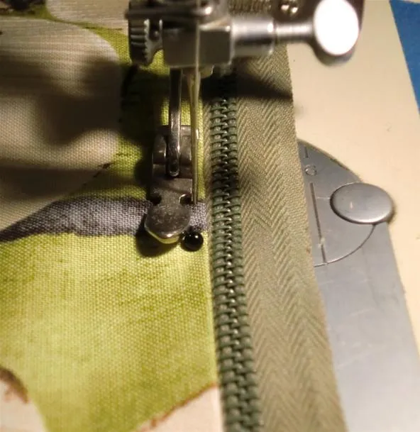 Close-up of a sewing machine foot stitching a green zipper.