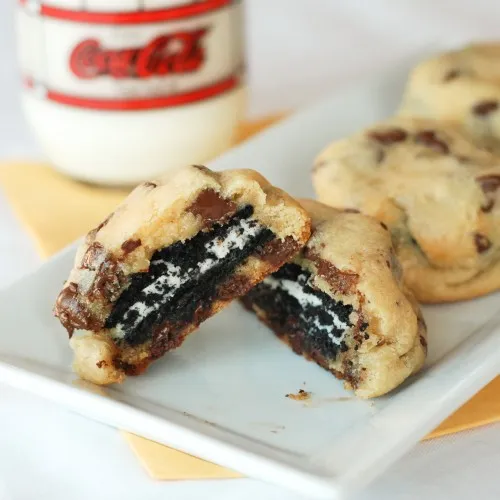 Chocolate chip cookies stuffed with Oreo cookies, served with a glass of milk.