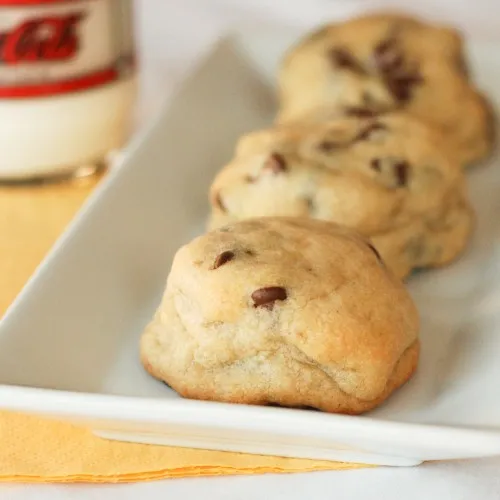 Chocolate chip cookies on a white platter with a glass of milk in the background.
