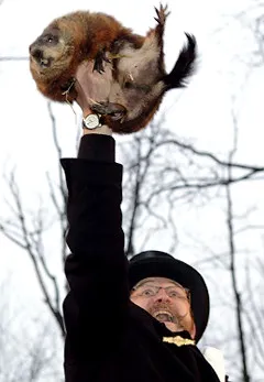 Man holding a groundhog aloft outdoors.