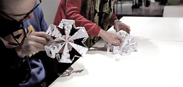People constructing intricate paper models at a table.