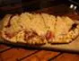 Person preparing pizza with toppings on a wooden countertop.