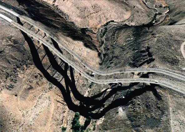 Aerial view of a winding road and river through mountainous terrain.