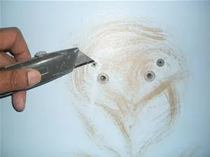 Person using a utility knife on a wall with visible repair spots.