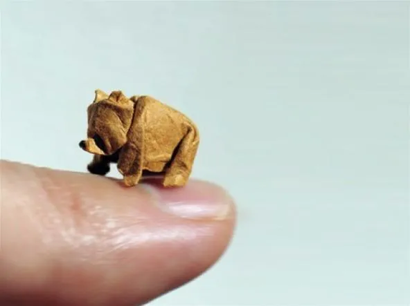 A tiny origami bear sitting on a fingertip.