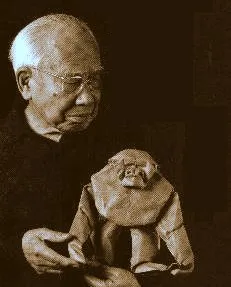 An elderly man holding a handmade monkey sculpture.