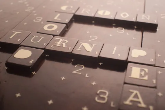 Scrabble pieces spelling "CROON," "TURNIP," and "LONE" on a wooden surface.