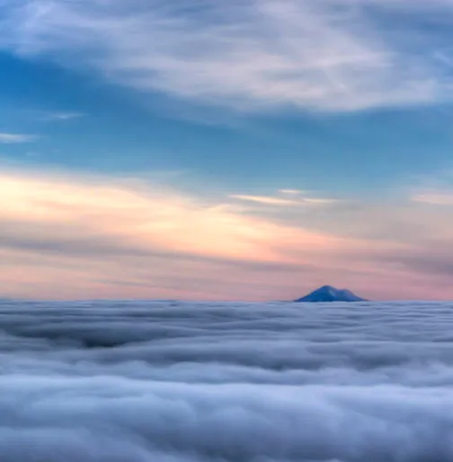 Clouds under a colorful sky with a mountain peak visible in the distance.
