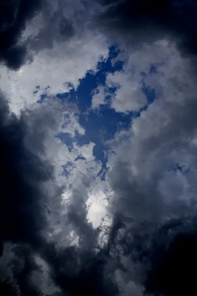 Dramatic cloud formations with a break revealing blue sky.