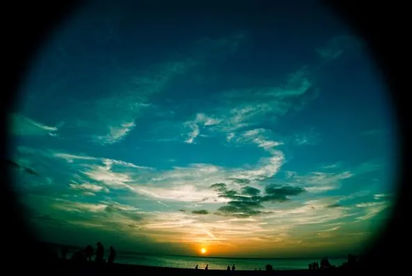 Sunset over calm ocean waters with colorful clouds and silhouetted figures on the shore.