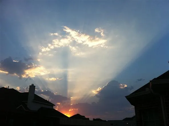 Sunset with vibrant rays of light breaking through clouds over rooftops.