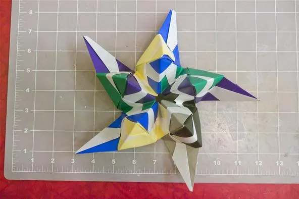 Colorful origami star with geometric shapes on a cutting mat.