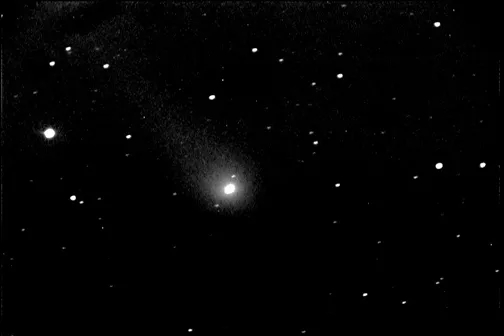 Bright comet with a distinct tail surrounded by stars in a night sky.