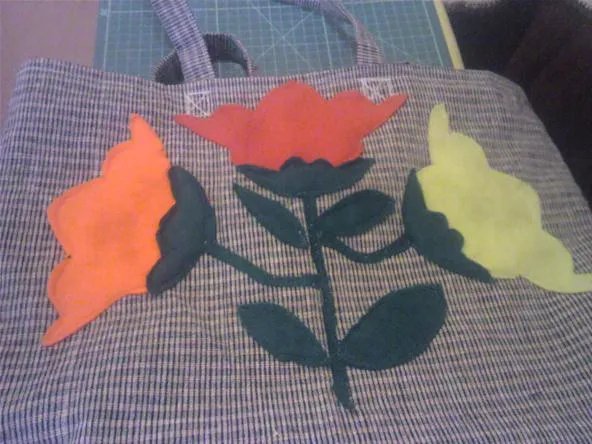 Colorful felt flower appliqué design on a textured fabric handbag.
