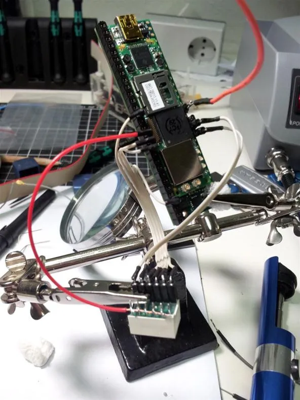 A circuit board and components being soldered on a workbench with magnifying tools.