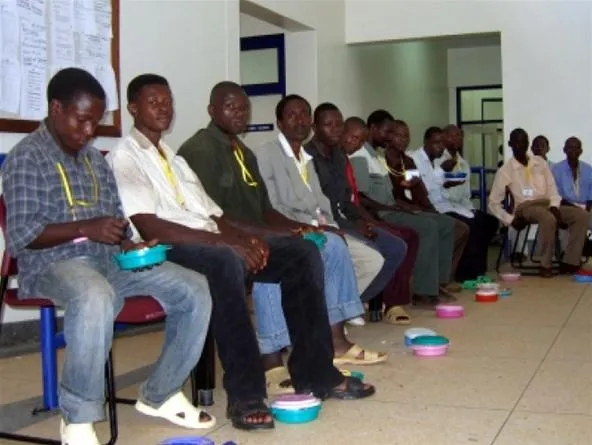 Men sitting in a row with bowls in a communal space.